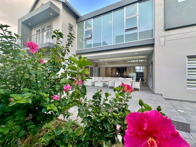 Modern rear elevation featuring a spacious tiled patio, large glass windows, and an upper-level balcony, seamlessly connecting indoor and outdoor living spaces.