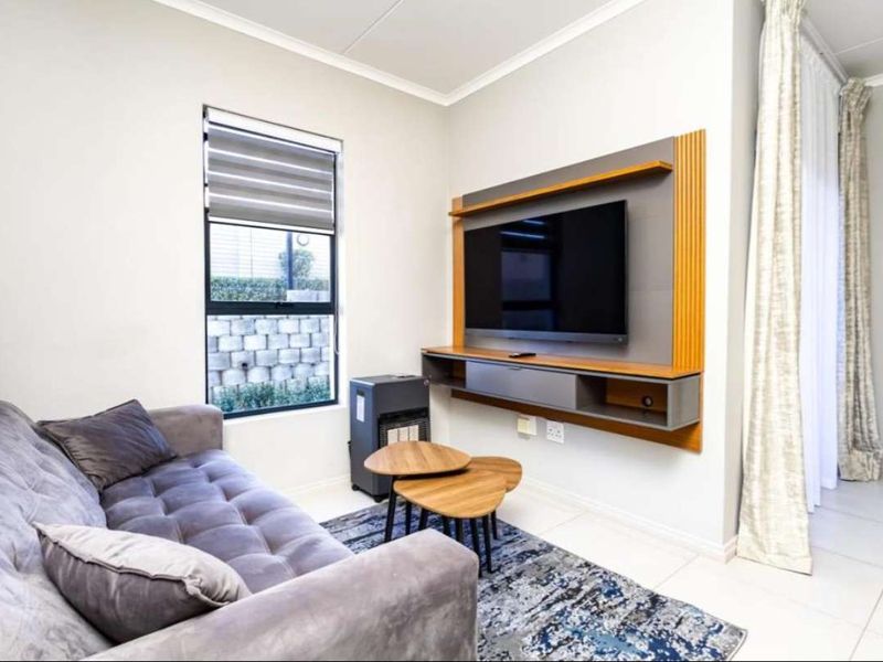 A well-maintained living room featuring tiled flooring, a modern built-in media console, and large windows with roller blinds and curtain tracks.