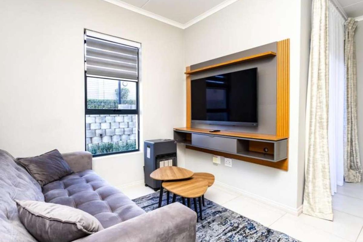 A well-maintained living room featuring tiled flooring, a modern built-in media console, and large windows with roller blinds and curtain tracks.