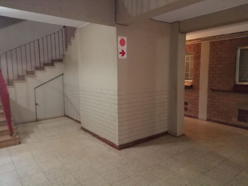 A communal apartment hallway featuring a staircase with metal balustrade and exposed brick wall sections, showing signs of wear and dated finishes.