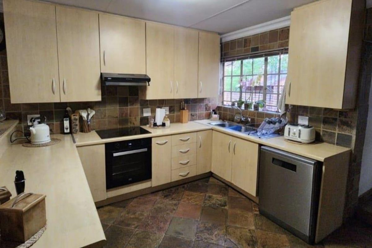 A functional kitchen featuring light wood cabinetry, stone-tiled splashbacks, a built-in oven, hob, extractor fan, and durable stone flooring.