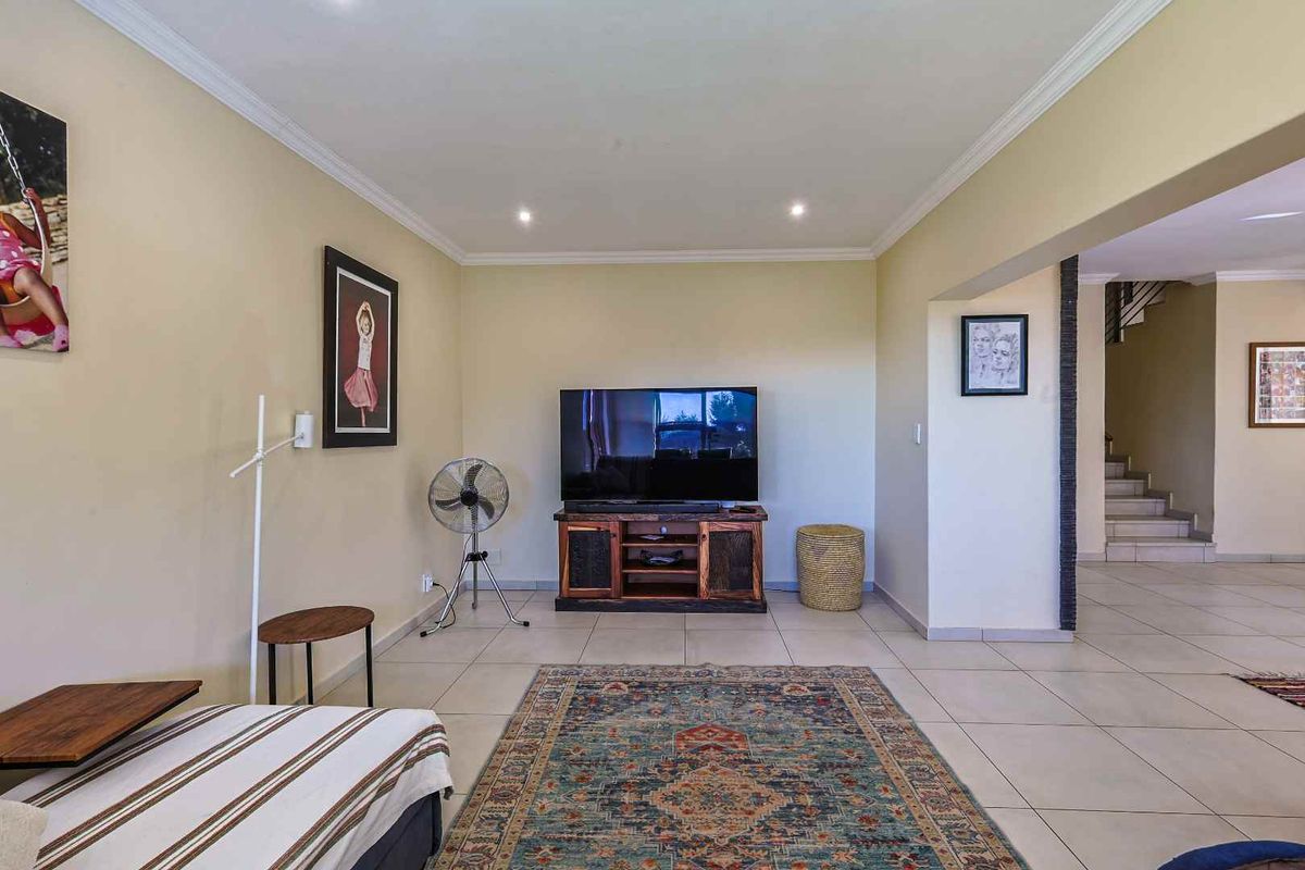 A spacious living room featuring neutral tiled flooring, recessed ceiling lighting, and a transition area leading to a staircase.