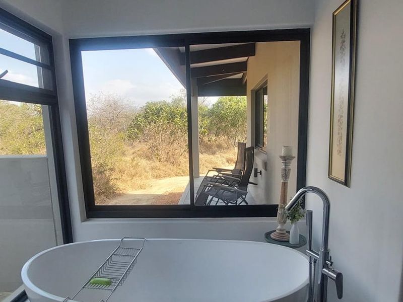 Modern bathroom featuring a sleek freestanding bathtub with a floor-mounted faucet and large windows offering scenic views of the outdoor patio and landscape.
