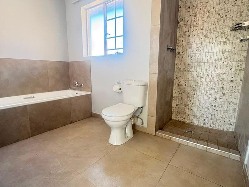 A spacious bathroom featuring a built-in bathtub, a separate walk-in shower with mosaic tiling, and neutral floor tiles.