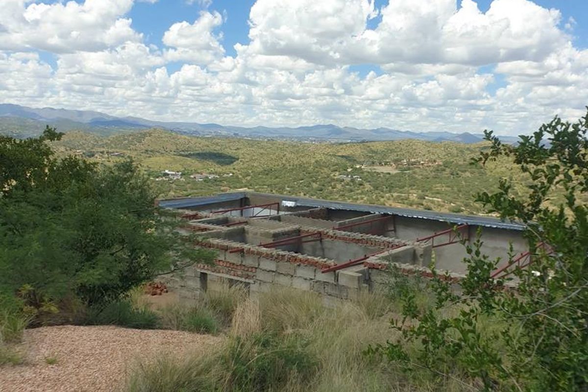 An elevated view of a residential property under construction, featuring exposed brickwork and steel roof framing set against a scenic landscape.