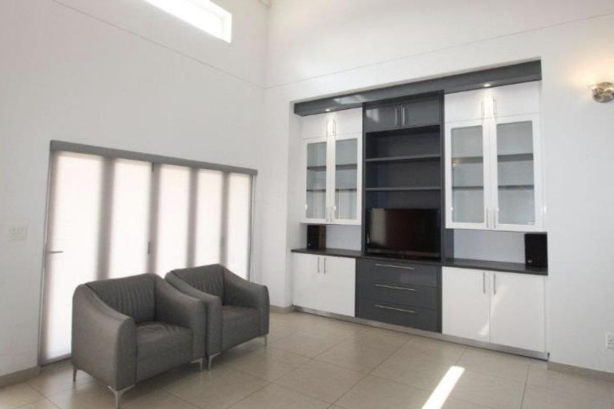 Spacious living room featuring high ceilings, large windows with blinds, and a modern, custom-built floor-to-ceiling entertainment unit with integrated cabinetry.