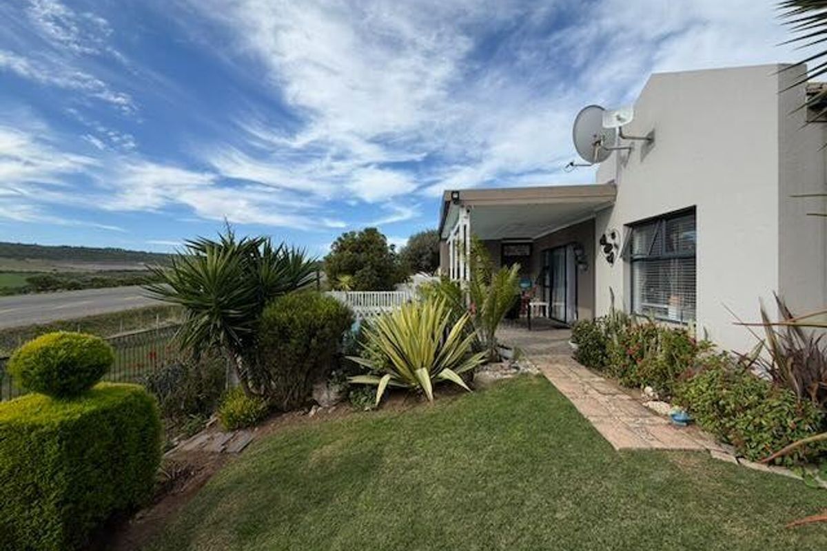 Rear view of the property featuring a covered patio, landscaped garden, and paved walkway with views of the surrounding landscape.
