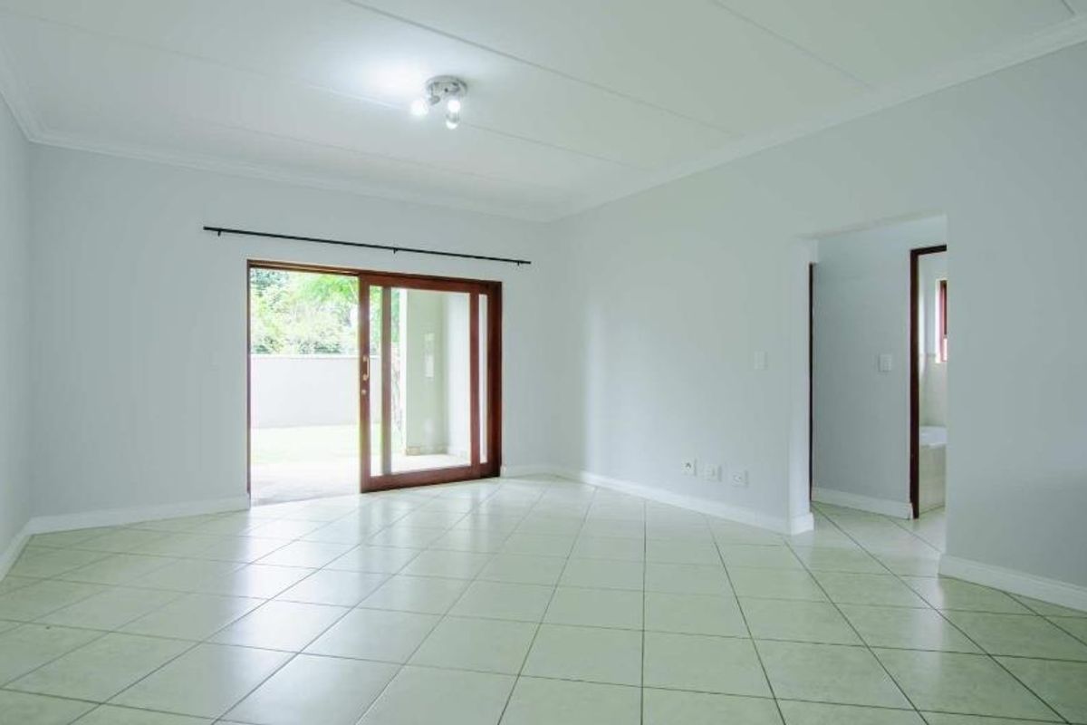 A bright, empty living room featuring neutral tiled flooring, coved ceilings, and a sliding glass door providing access to the outdoor area.