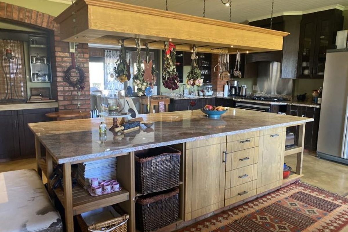 Spacious kitchen featuring a large central island with stone countertop, wooden cabinetry, and a suspended overhead rack for storage and lighting.