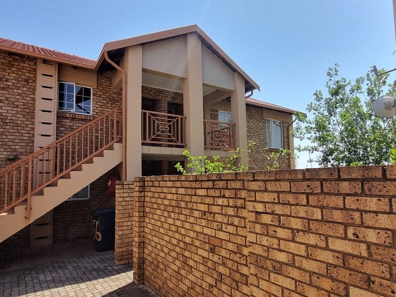Exterior view of an apartment complex featuring face brick construction, an external staircase with metal railings, and a paved entrance area.
