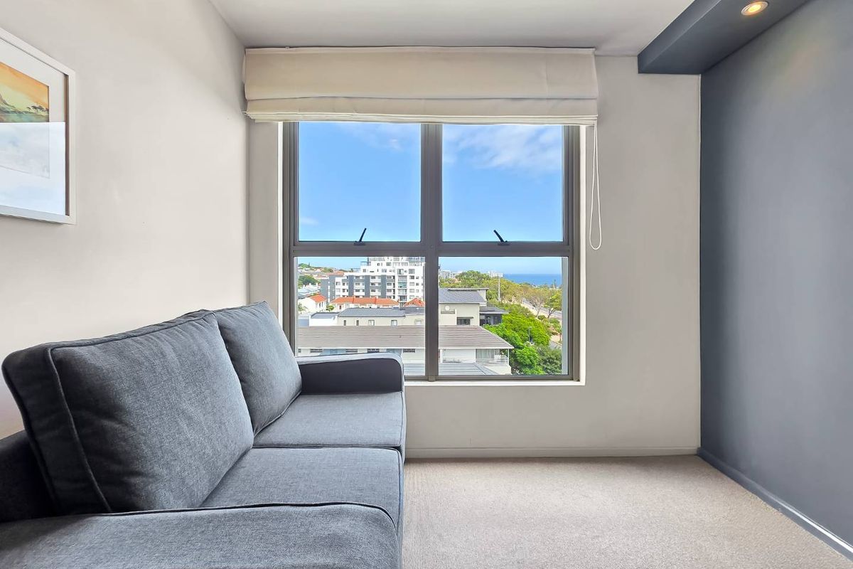 A bright living area featuring a large window with a roman blind, recessed ceiling lighting, and a pleasant urban view.