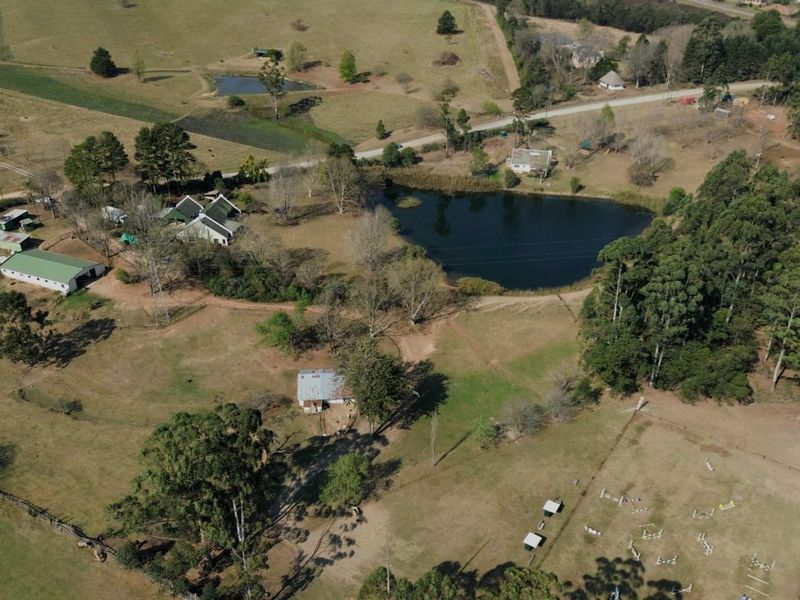 Aerial view of a large farm property featuring multiple outbuildings, a private dam, expansive paddocks, and established tree lines.