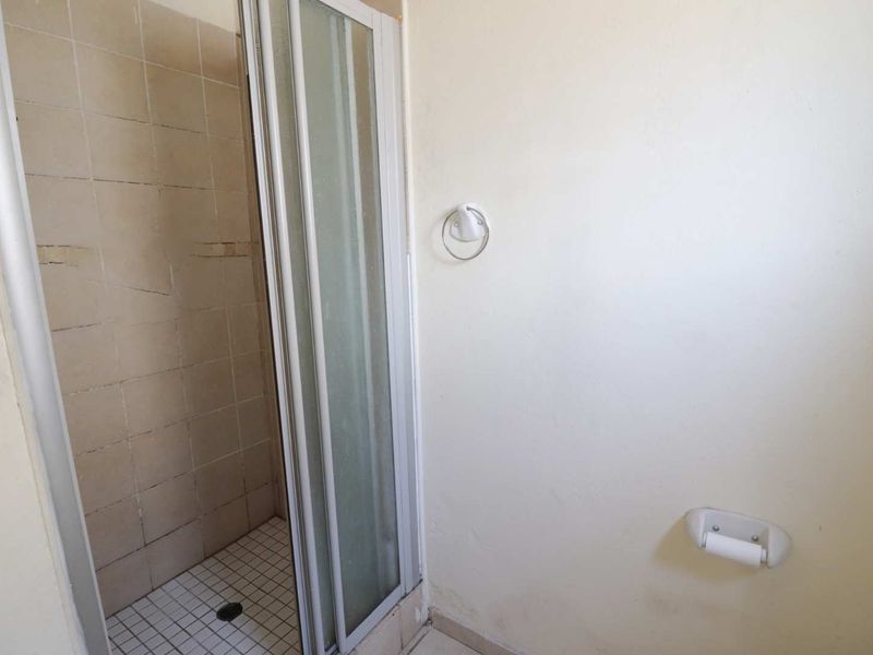 A functional bathroom featuring a shower enclosure with tiled walls and floor, equipped with basic wall-mounted fixtures.