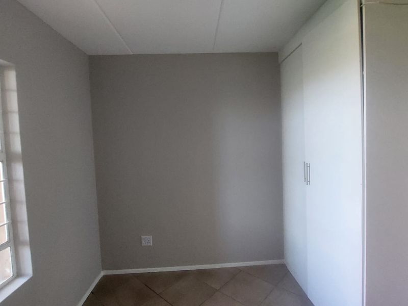 A clean, empty bedroom featuring neutral wall tones, tiled flooring, and practical built-in cupboards for storage.