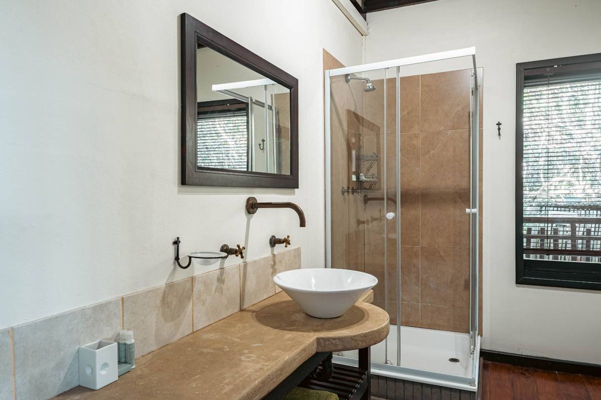 A bathroom featuring a vessel sink on a stone vanity, a glass-enclosed shower with brown wall tiles, and a framed wall mirror.