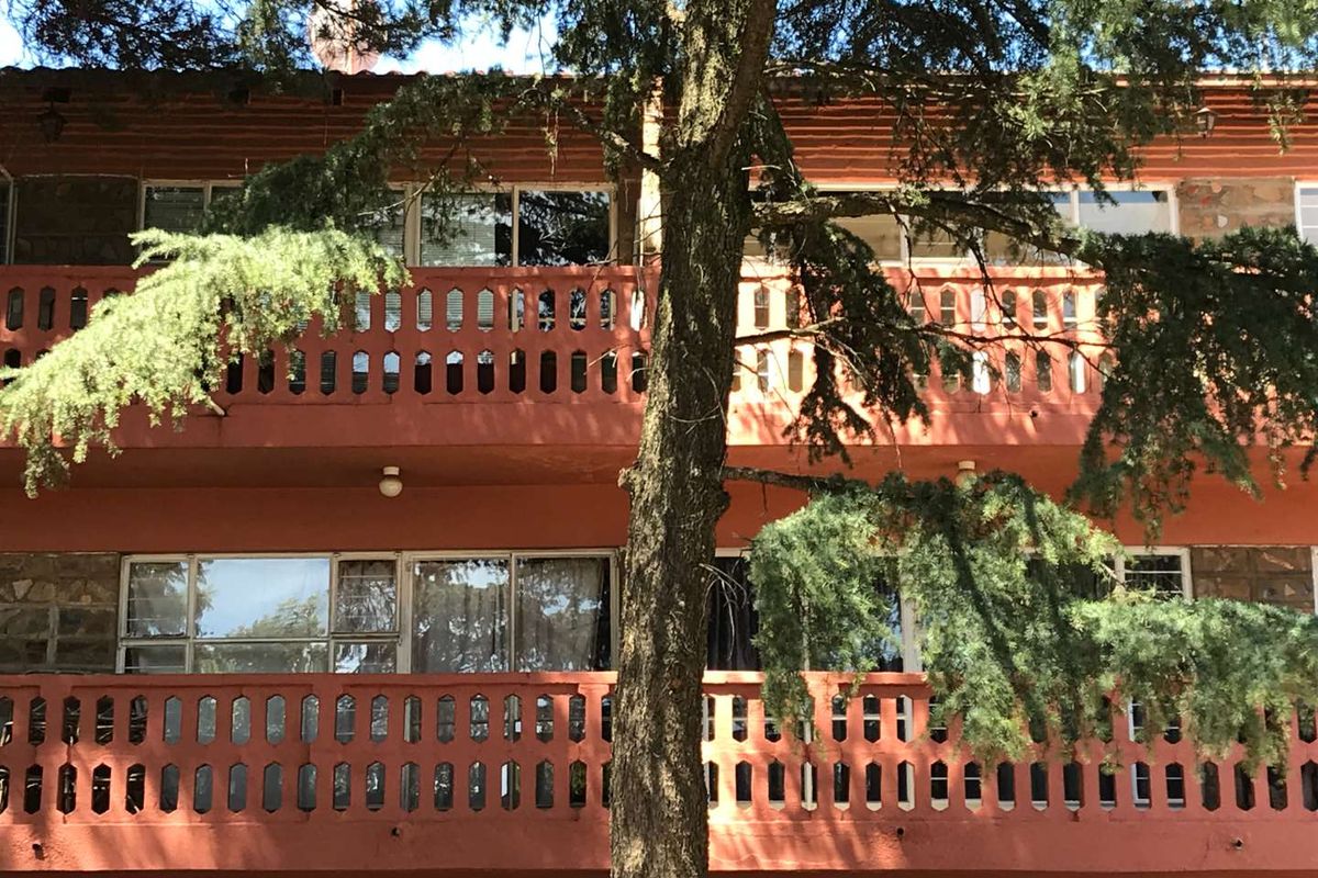 Exterior view of an apartment building featuring two levels of balconies with concrete balustrades and stone cladding facade details.
