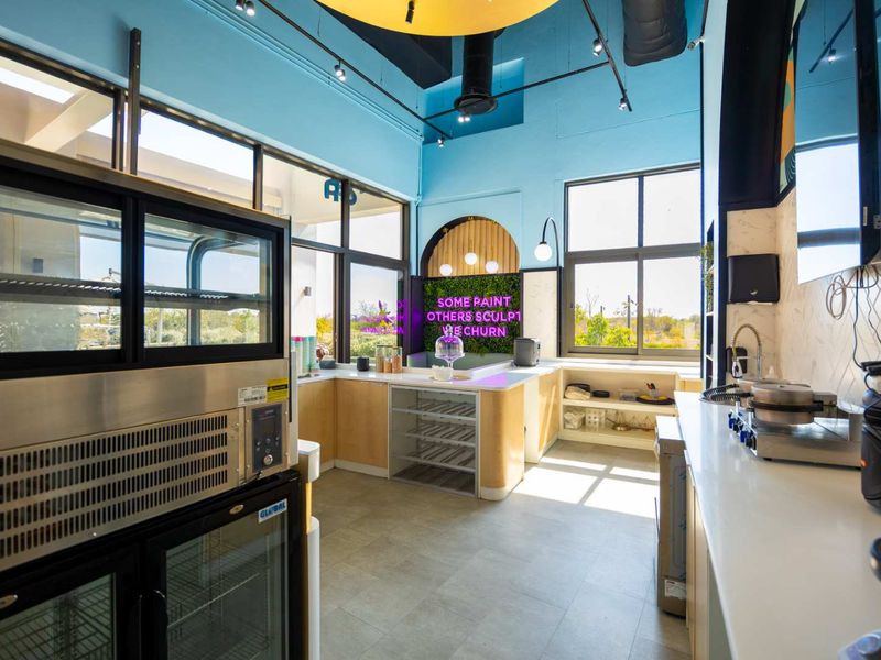 Modern commercial kitchen space featuring high ceilings, sleek cabinetry, stone countertops, and large windows providing ample natural light.