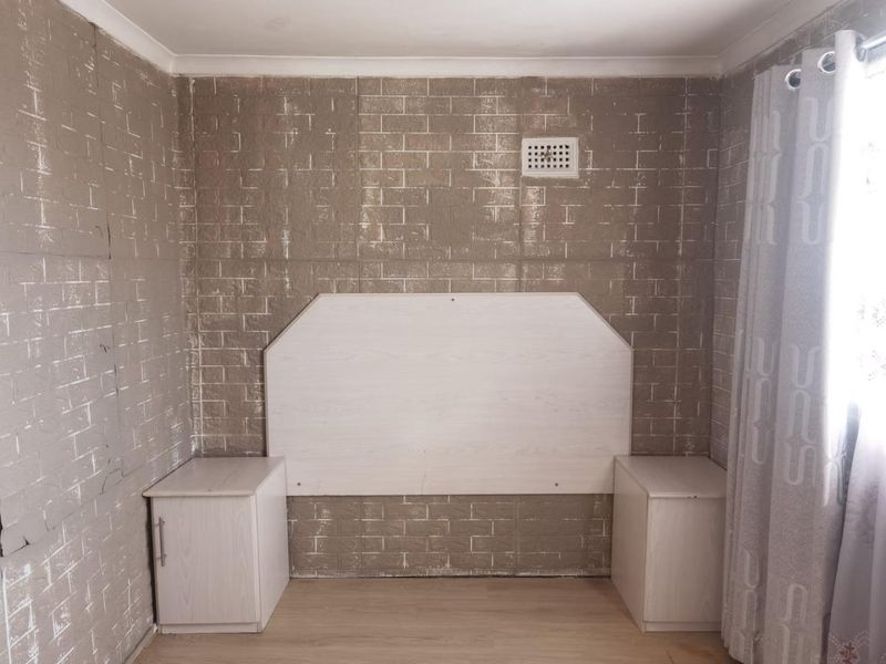 A bedroom featuring built-in bedside cabinetry and a headboard, finished with a textured brick-effect wall covering.