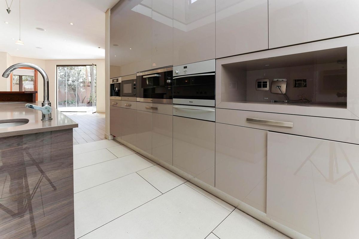 Modern kitchen featuring high-gloss cabinetry, integrated Miele appliances, stone countertops, and a central island with a sink, leading to an open-plan living area.