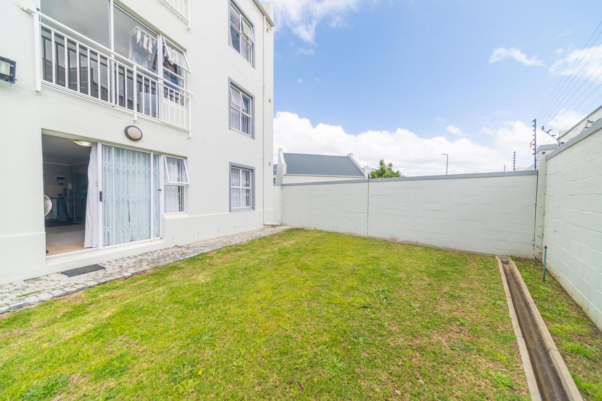 A private rear garden area featuring a small lawn, paved walkway, and direct access to the apartment via a sliding glass door.