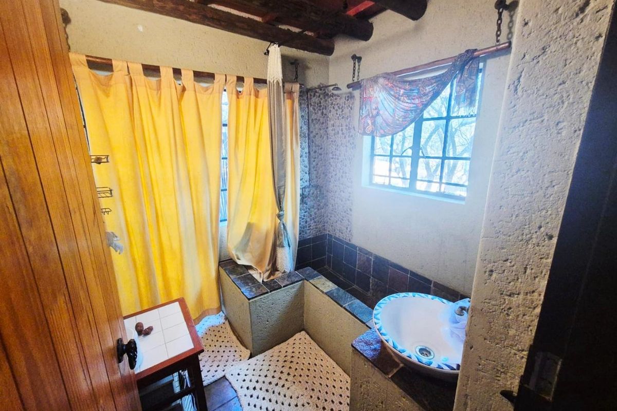 Rustic bathroom featuring a built-in tiled shower area, vessel sink, exposed timber ceiling beams, and textured wall finishes.