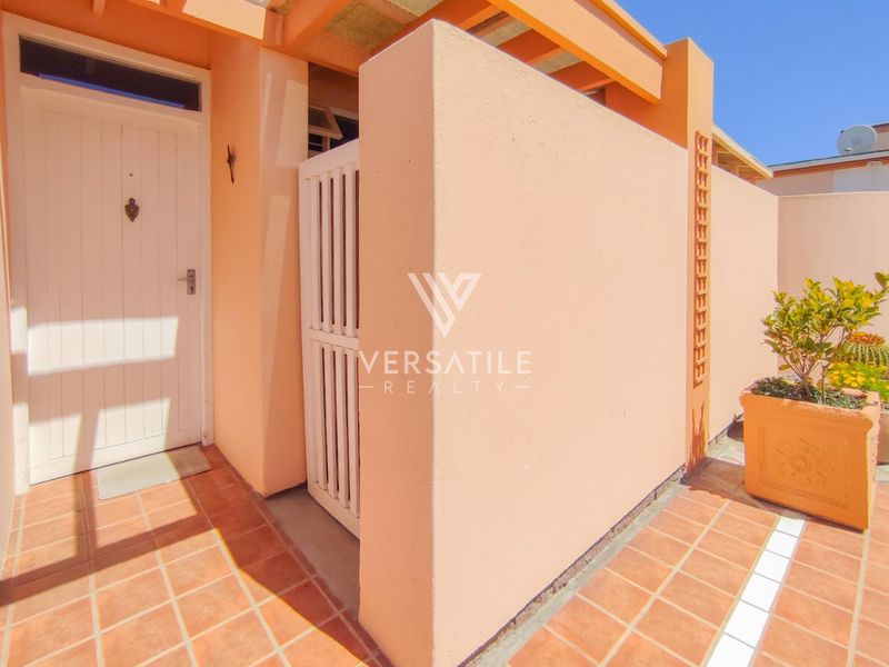 A well-maintained front entrance area featuring terracotta tiling, a secure gate, and a timber pergola structure.