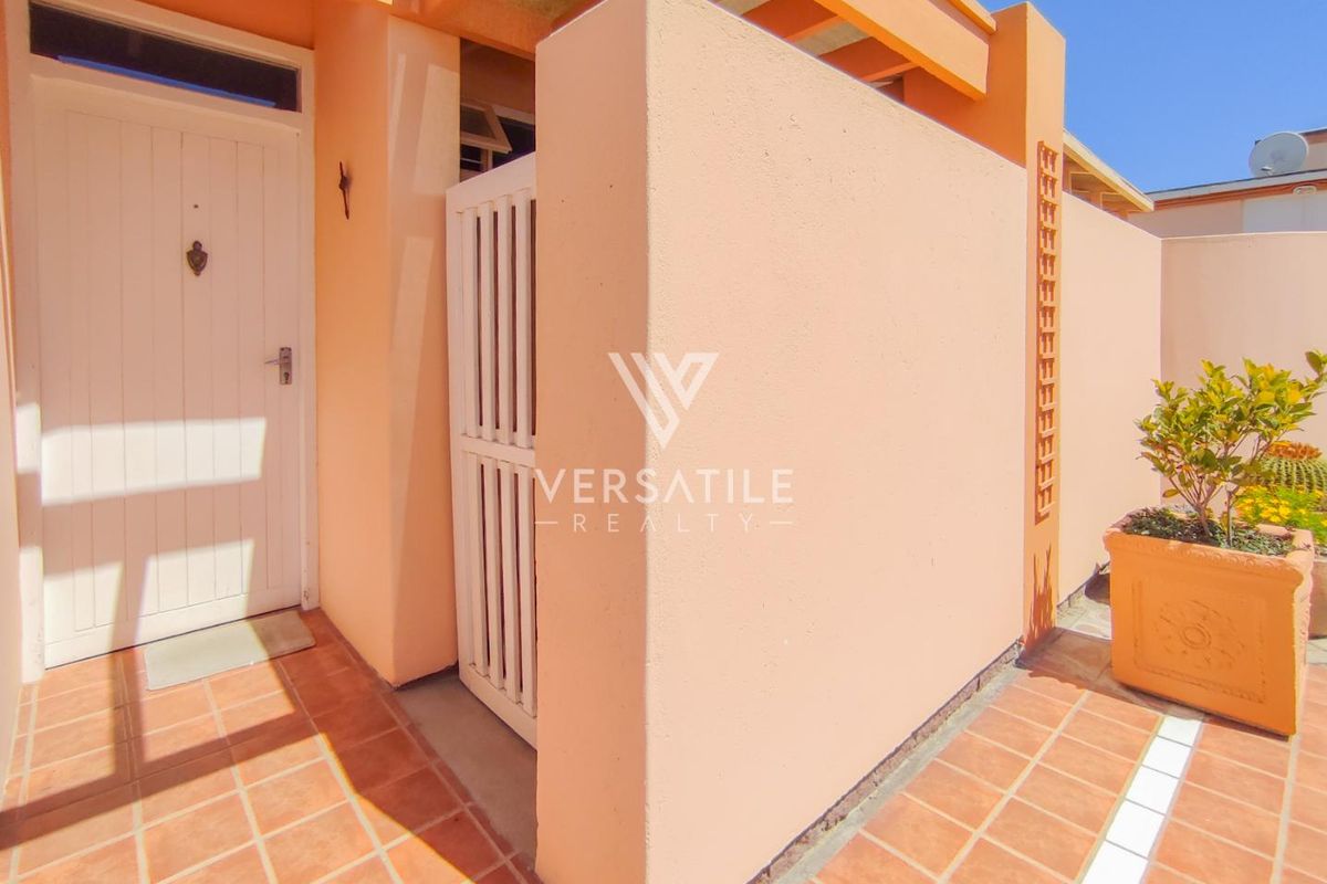 A well-maintained front entrance area featuring terracotta tiling, a secure gate, and a timber pergola structure.