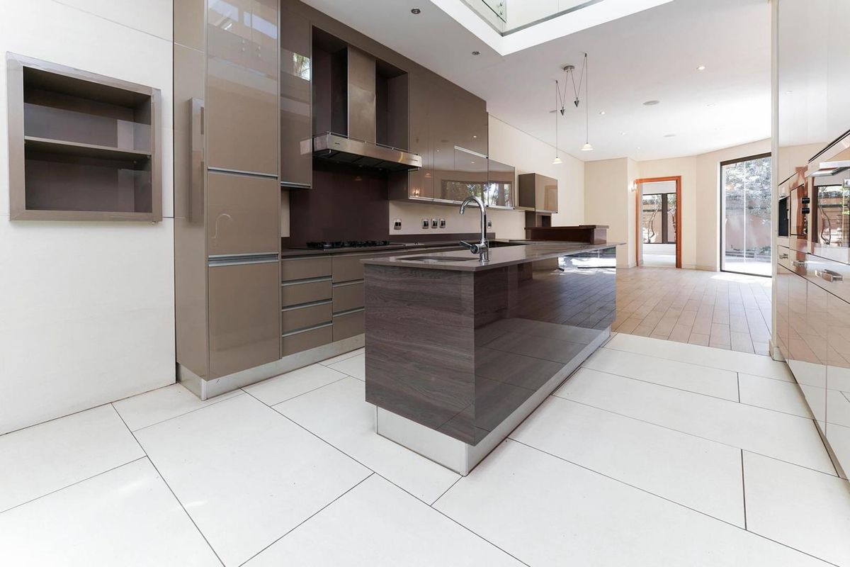 Modern, high-end kitchen featuring sleek cabinetry, a central island with an integrated sink, premium built-in appliances, and bright, tiled flooring under a skylight.