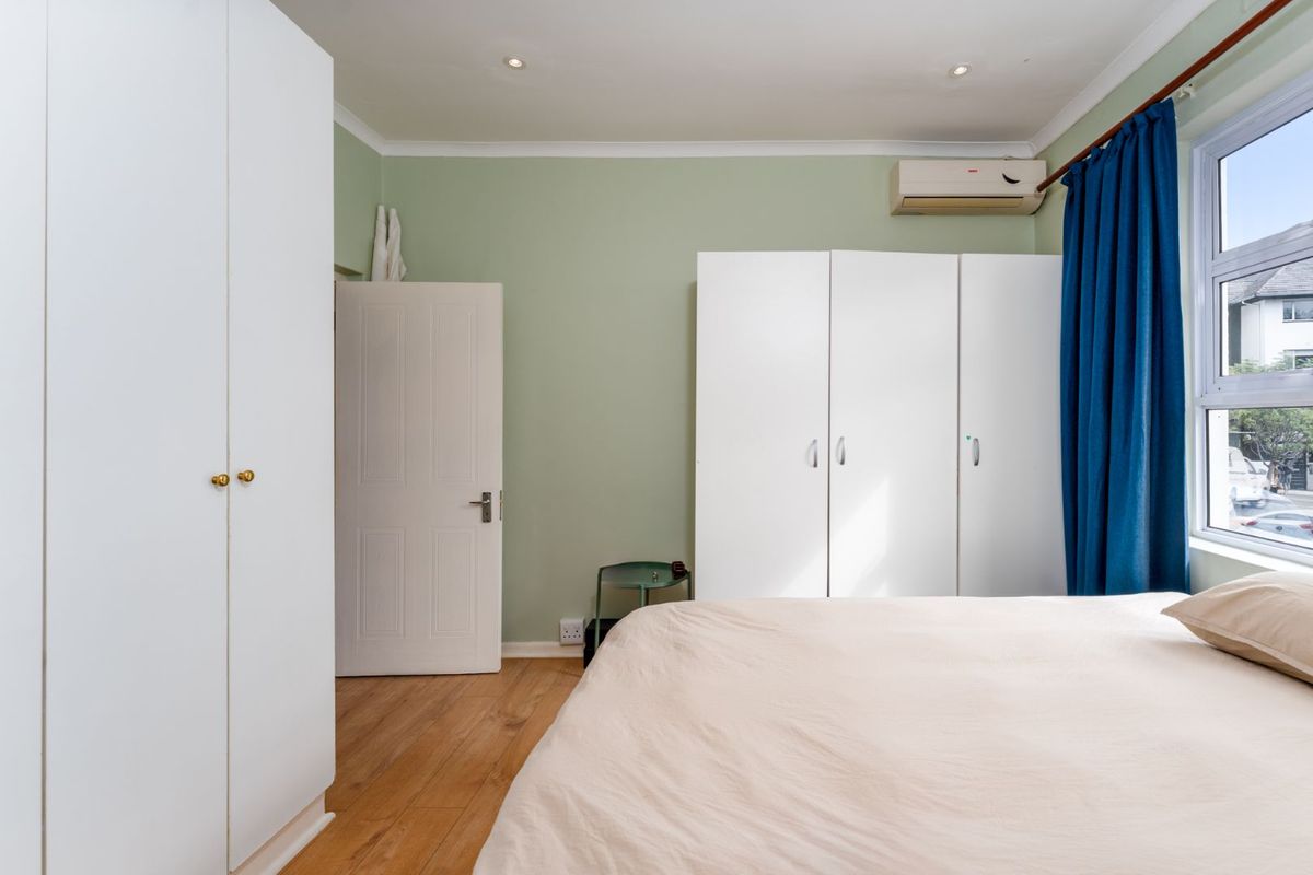A well-maintained bedroom featuring built-in wardrobes, laminate flooring, recessed ceiling lighting, and a wall-mounted air conditioning unit.