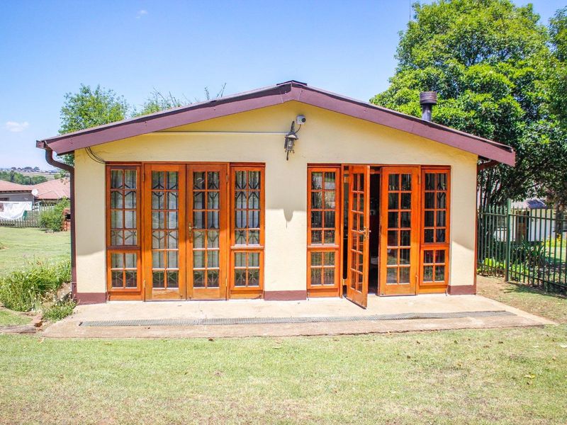 Rear view of a guest house featuring timber-framed french doors opening onto a concrete patio area set within a garden.