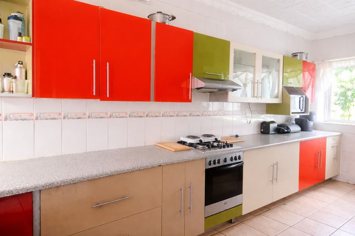 A functional kitchen featuring a mix of vibrant orange and green cabinetry, granite-look countertops, a built-in oven, gas hob, and extractor fan.