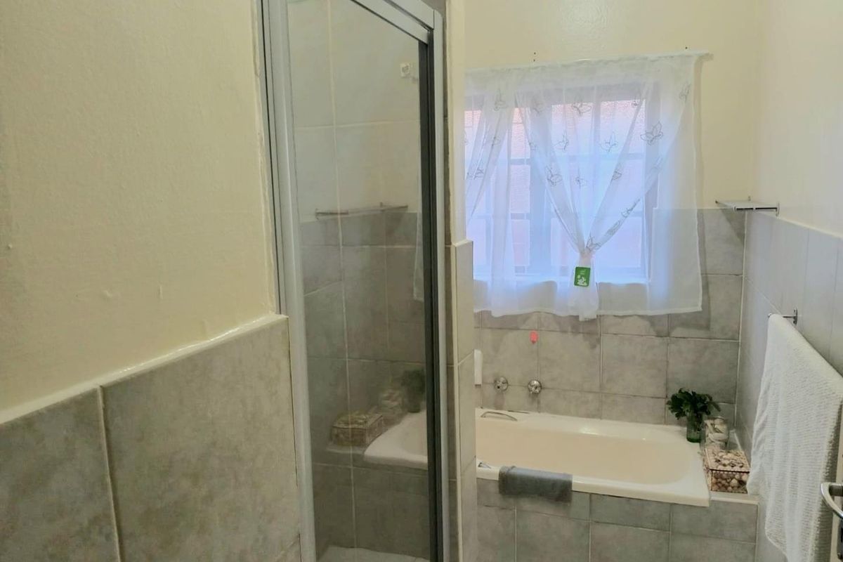 A functional bathroom featuring a built-in bathtub, a separate shower enclosure, and neutral wall tiling.