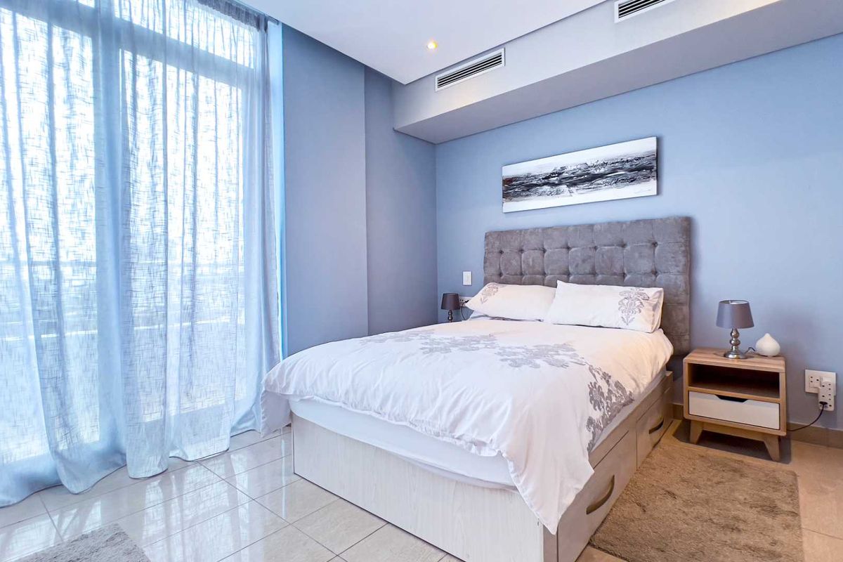 A well-maintained bedroom featuring tiled flooring, ducted air conditioning, and large glass sliding doors providing ample natural light.