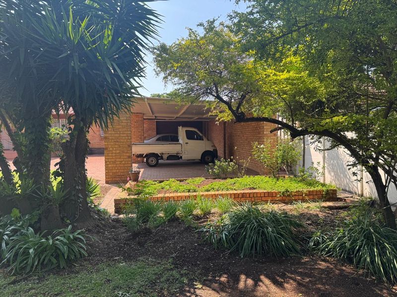 A functional brick carport structure with a paved driveway, situated within a landscaped garden setting.