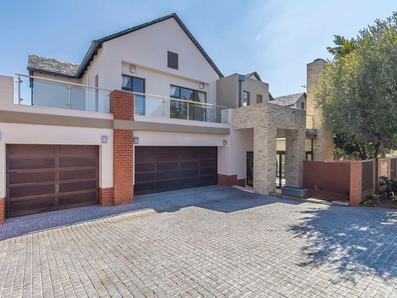 Modern double-storey residence featuring a paved driveway, double garage, and an upper-level balcony with glass balustrades and stone-clad architectural detailing.