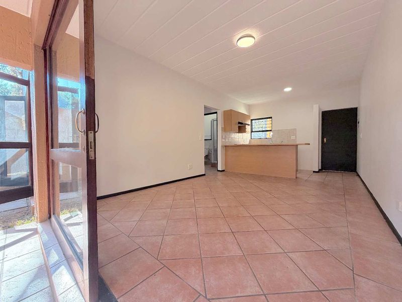 Open plan living area featuring tiled flooring, a functional kitchen with breakfast bar, and direct access to an outdoor space via sliding glass doors.