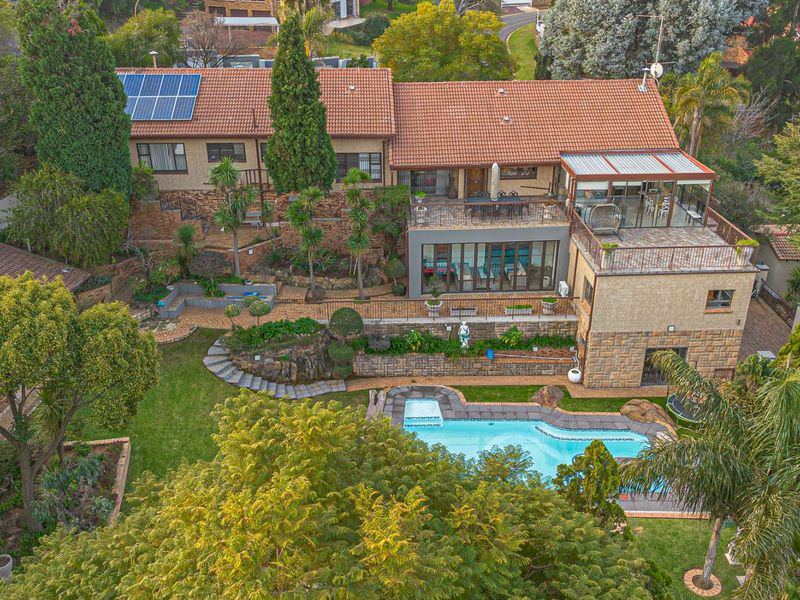Aerial view of a multi-level residential property featuring a swimming pool, landscaped terraced gardens, a spacious rear patio, and solar panels on the roof.