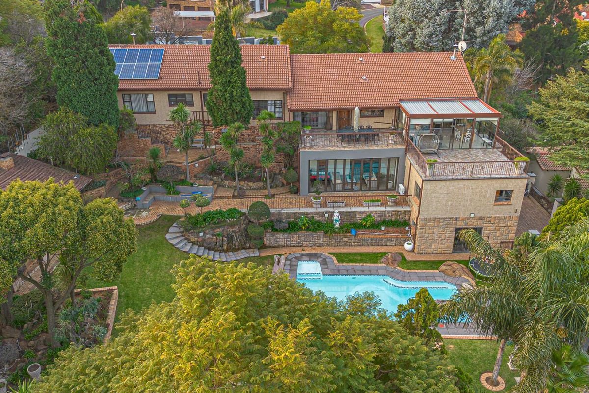 Aerial view of a multi-level residential property featuring a swimming pool, landscaped terraced gardens, a spacious rear patio, and solar panels on the roof.