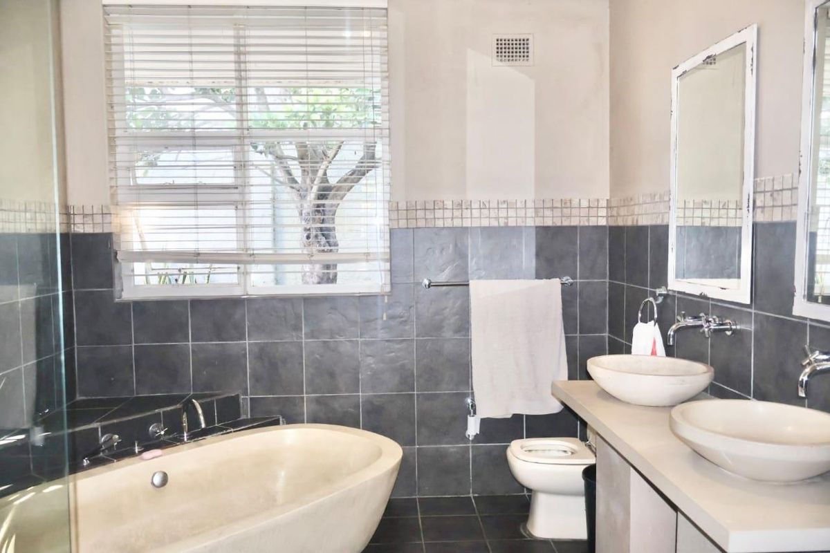 A bathroom featuring a double vanity with vessel sinks, a built-in bathtub, and dark tiled walls with a mosaic border.