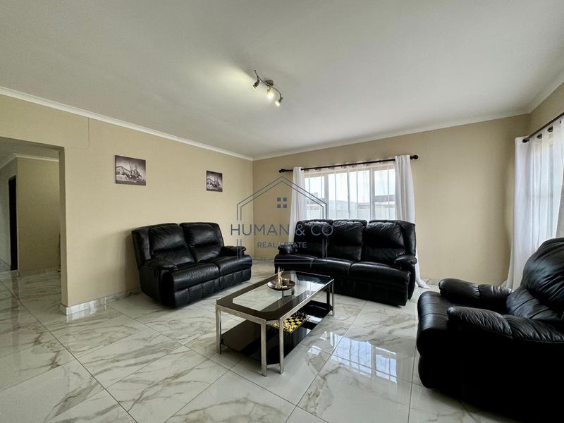 A spacious living room featuring polished marble-look floor tiles, neutral wall tones, and ample natural light through large windows.