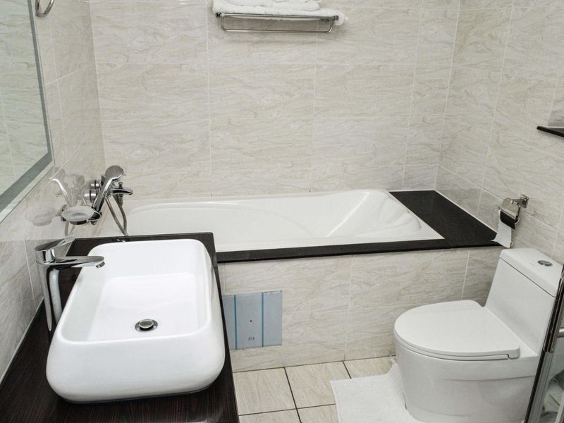 A modern bathroom featuring a built-in bathtub, vessel sink, chrome fixtures, and neutral tiled finishes throughout.