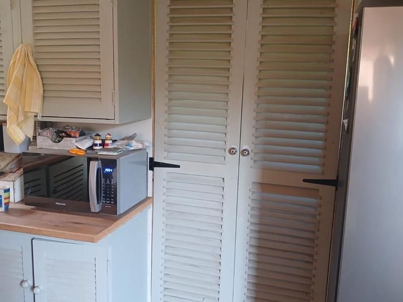 A kitchen area featuring louvered cabinetry and a wooden countertop, with visible unfinished trim and structural elements around the doorway.