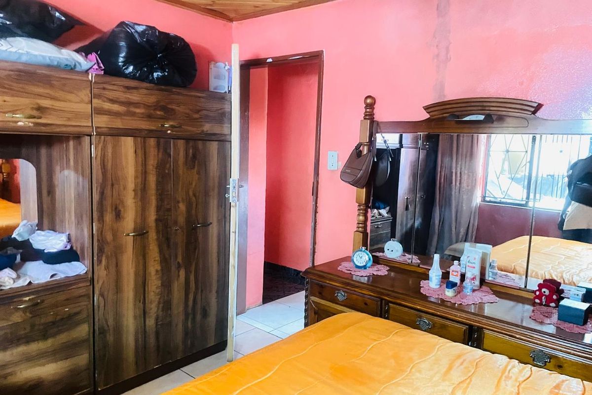 A bedroom featuring built-in wooden cabinetry and a timber-paneled ceiling, showing signs of wear and water staining on the wall.