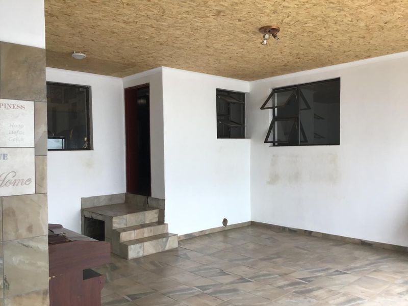 An open-plan covered patio area featuring tiled flooring, an OSB ceiling, and a built-in braai, offering a versatile space for outdoor entertainment.