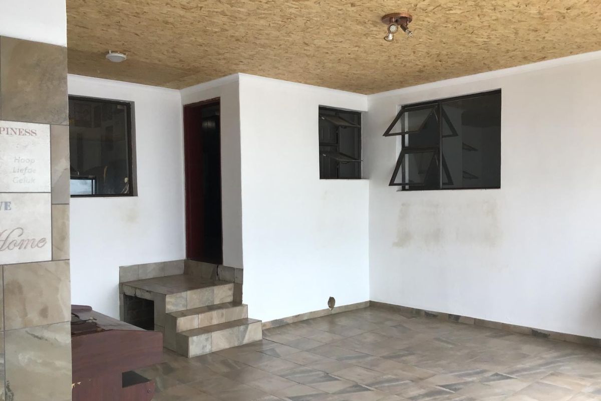An open-plan covered patio area featuring tiled flooring, an OSB ceiling, and a built-in braai, offering a versatile space for outdoor entertainment.