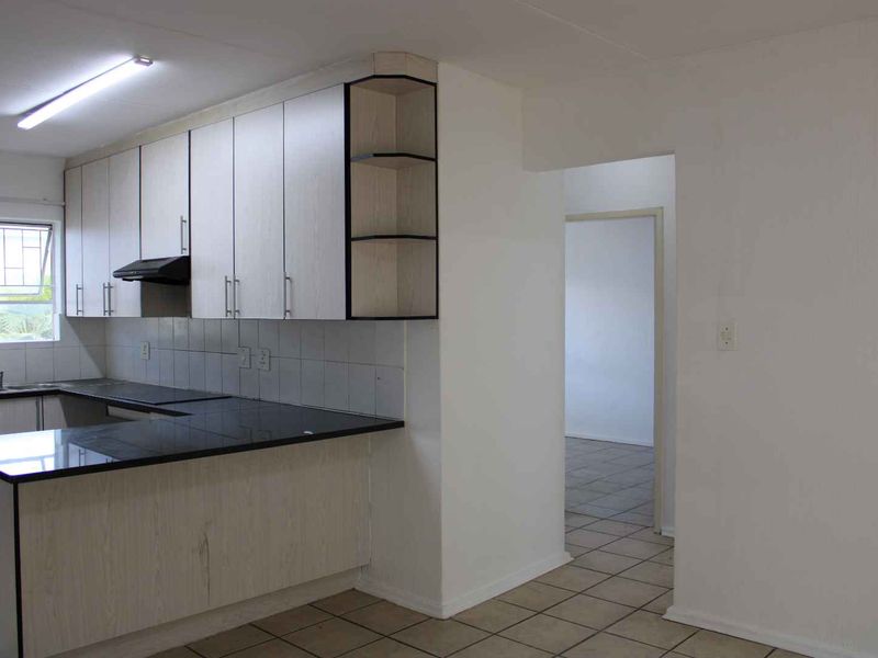 Functional kitchen featuring light-toned cabinetry, dark countertops, tiled backsplash, and integrated extractor fan, leading into an adjacent living area.