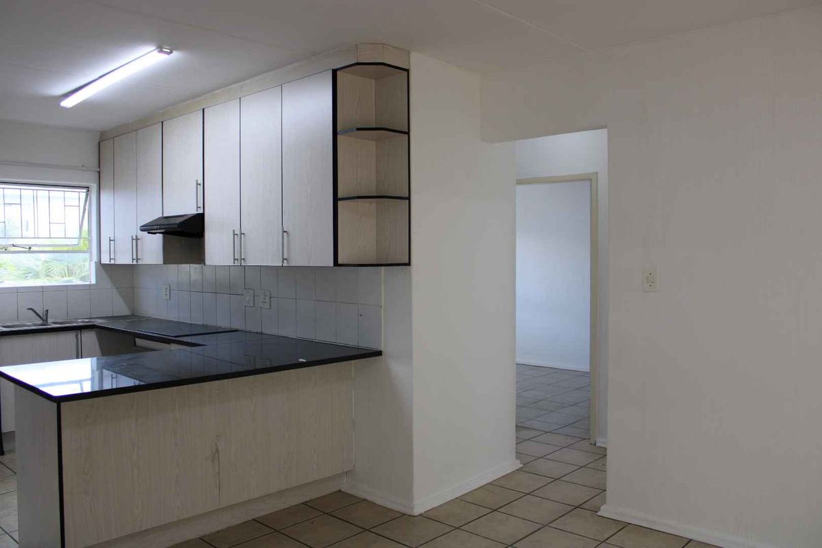 Functional kitchen featuring light-toned cabinetry, dark countertops, tiled backsplash, and integrated extractor fan, leading into an adjacent living area.