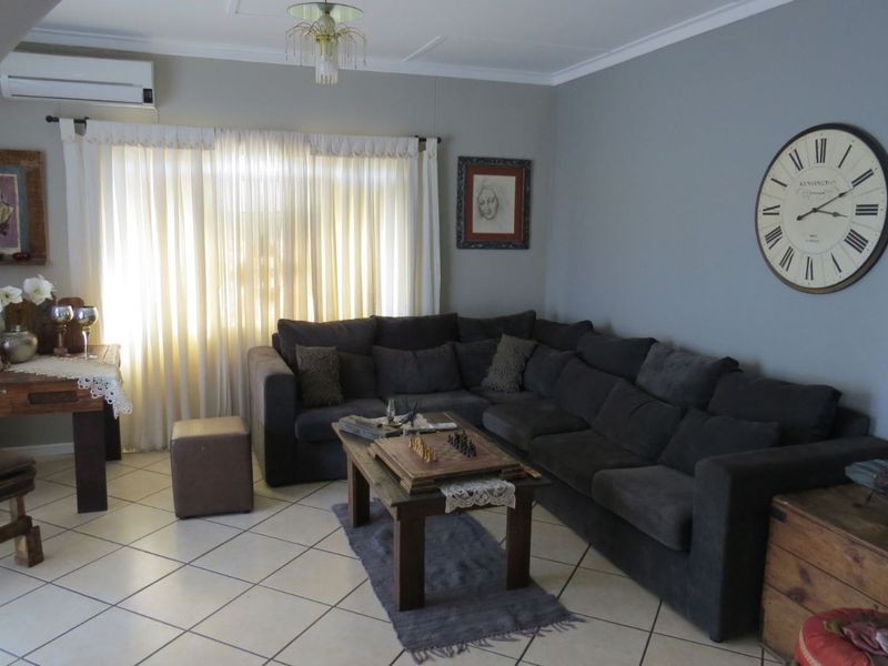A comfortable living room featuring tiled flooring, a wall-mounted air conditioning unit, and large windows with curtains.