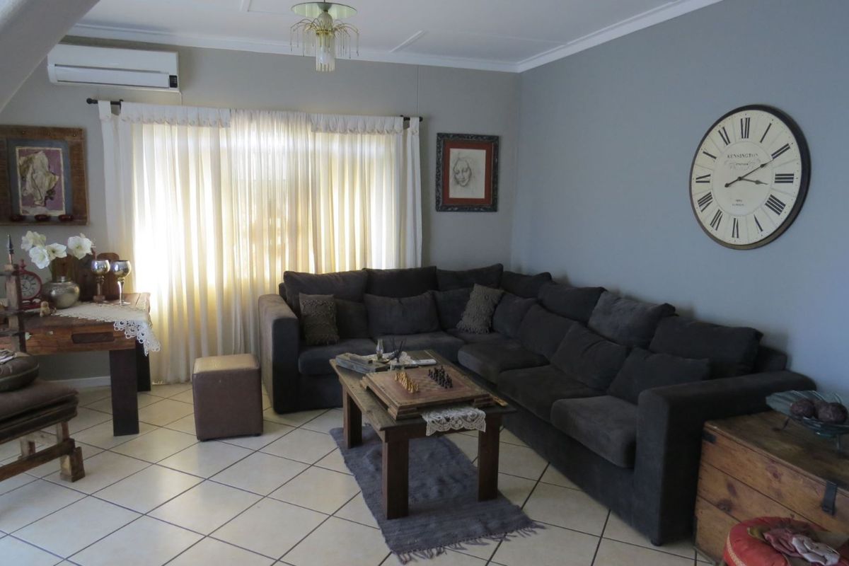A comfortable living room featuring tiled flooring, a wall-mounted air conditioning unit, and large windows with curtains.