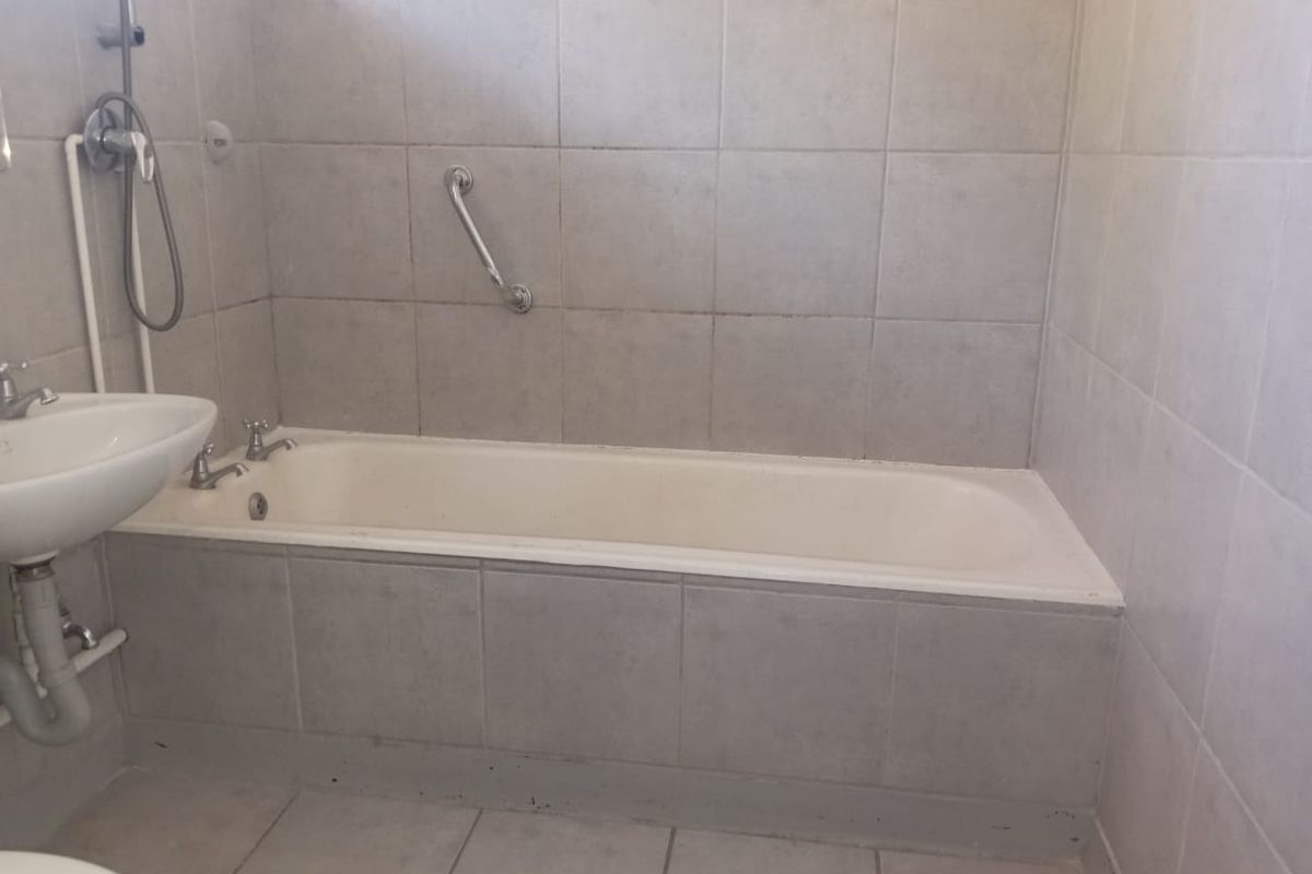 A functional bathroom featuring a bathtub with a shower mixer, pedestal basin, and neutral ceramic tiling throughout.